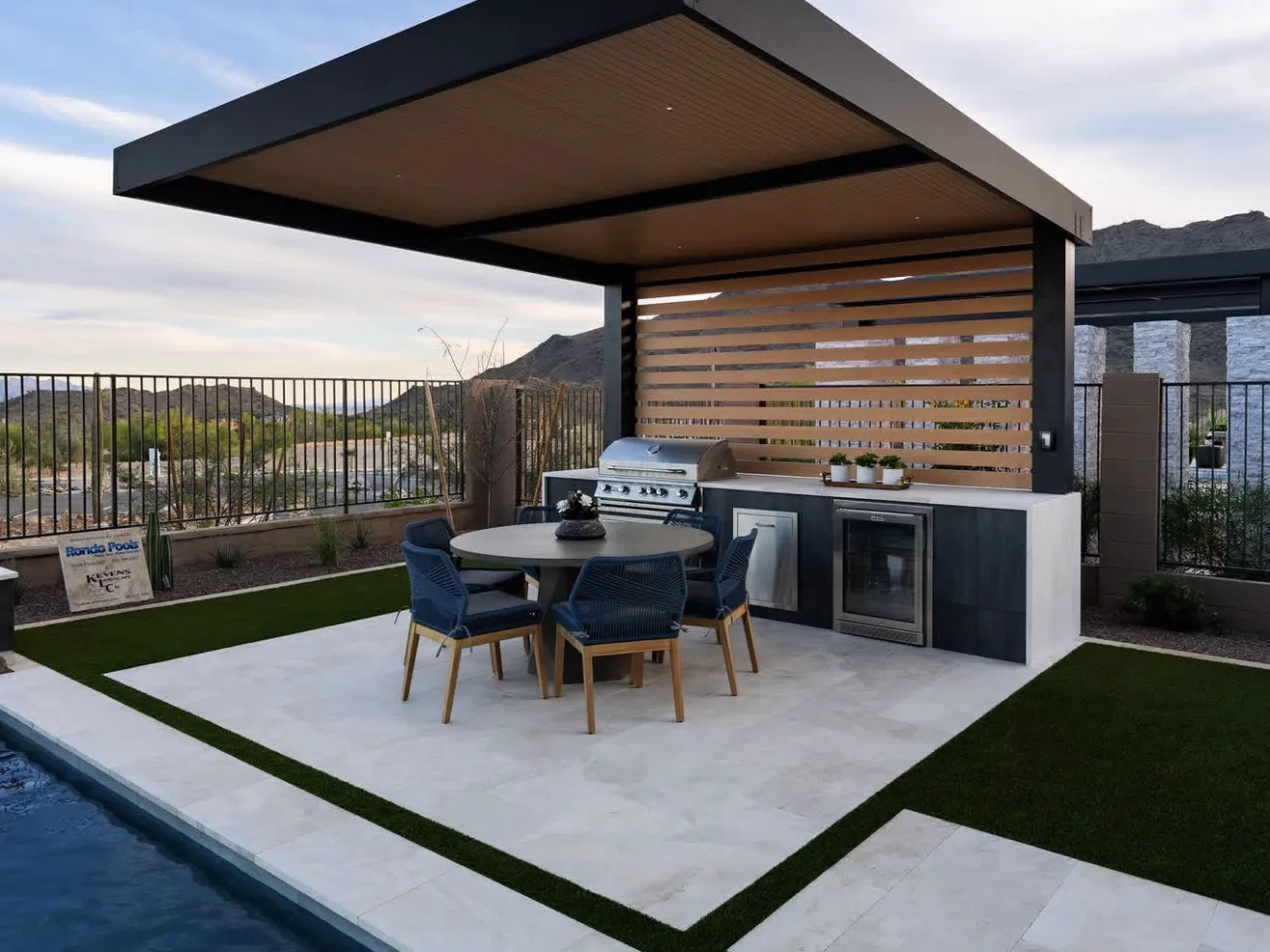 Hard top with a warm timber soffit over an outdoor kitchen and dining table, mountains beyond — photograph