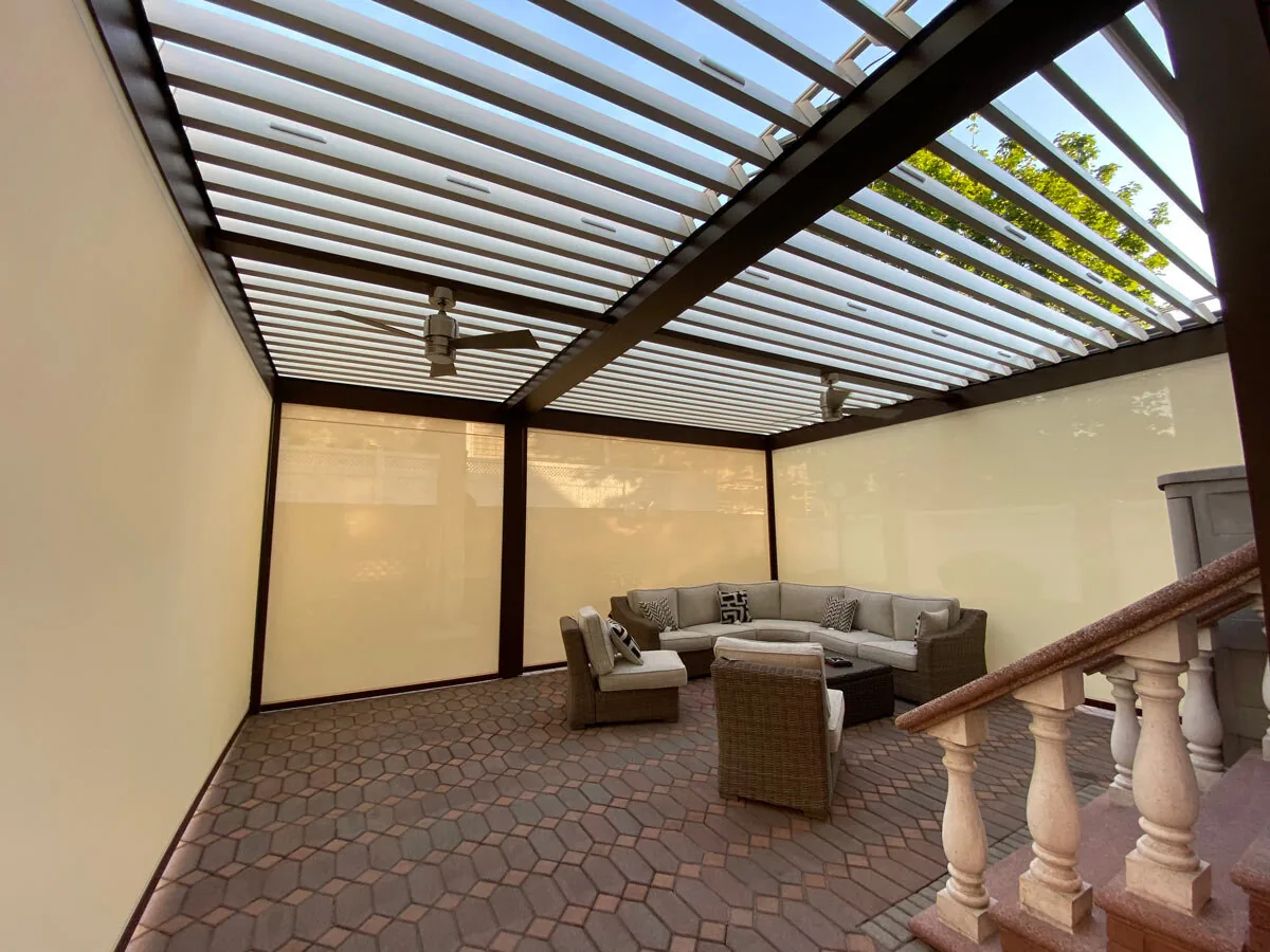 Under the courtyard pergola with zip screens lowered on two sides and ceiling fans below the open blades — photograph