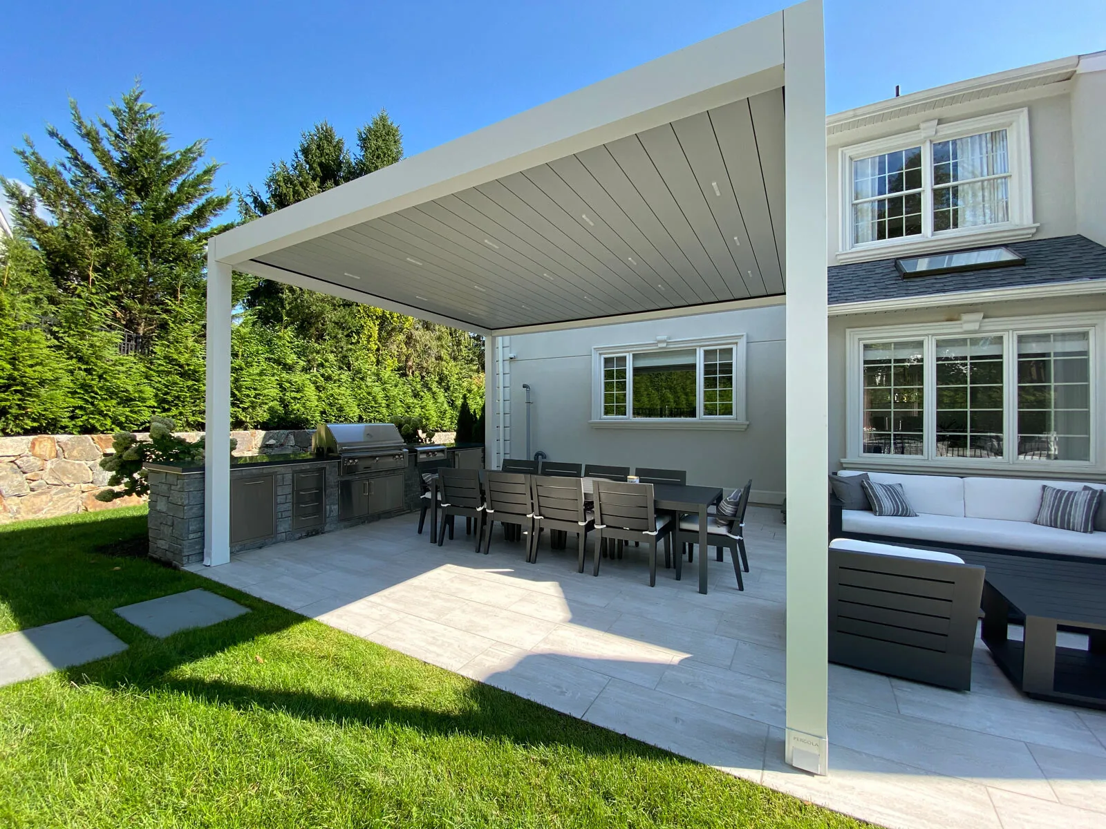 The same white-framed pergola seen from the lawn, closed roof, stone-clad outdoor kitchen beneath — photograph