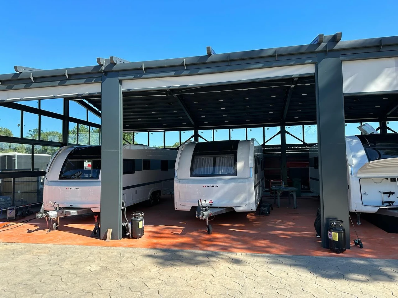 A wide exterior view of a dark supported fabric canopy and side screens above parked caravans.