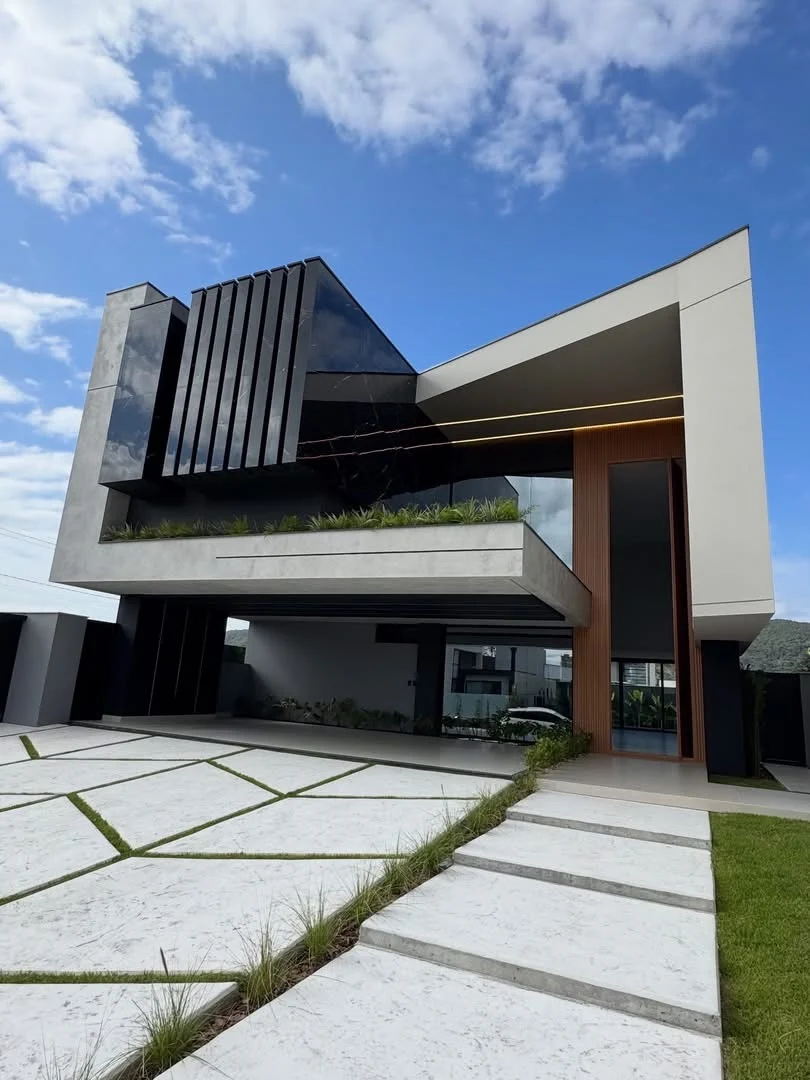 An angular residential facade with a deep white perimeter frame, dark glazing, vertical fins and a planted terrace.