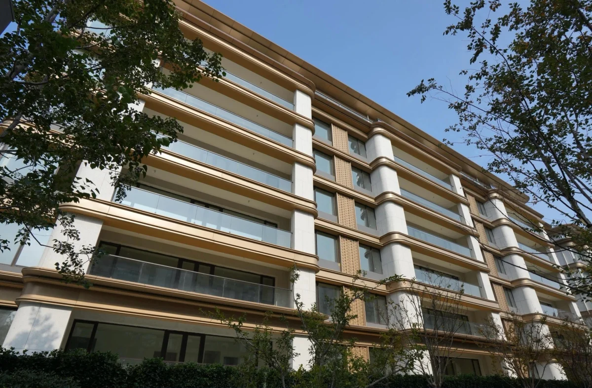Wide oblique view of a pale stone residential facade with bronze horizontal bands, glass balconies and patterned screens.