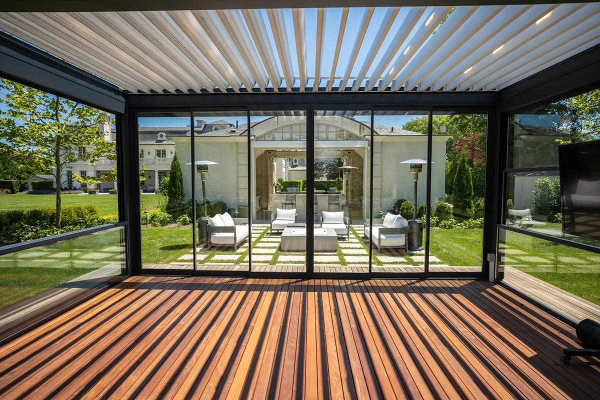 Architectural concept with white open louvers above a glazed garden room, looking across a wooden deck toward outdoor seating.